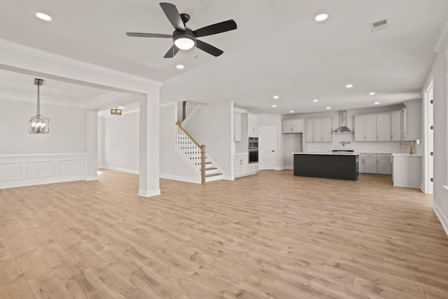 unfurnished living room with stairs, visible vents, ornamental molding, light wood-type flooring, and ceiling fan with notable chandelier