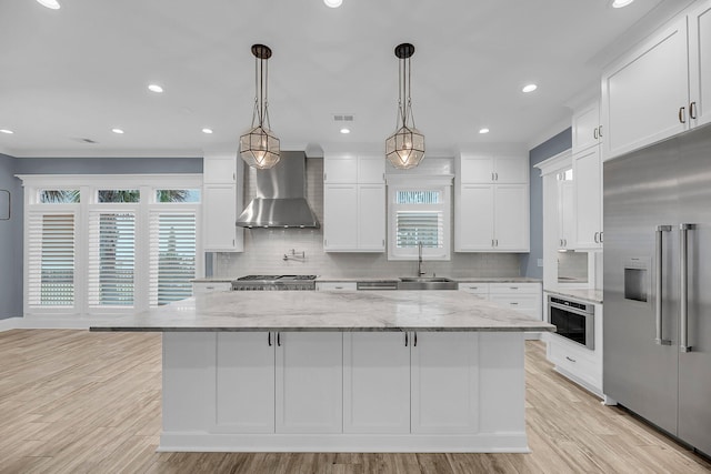 kitchen with visible vents, a sink, stainless steel appliances, white cabinetry, and wall chimney range hood