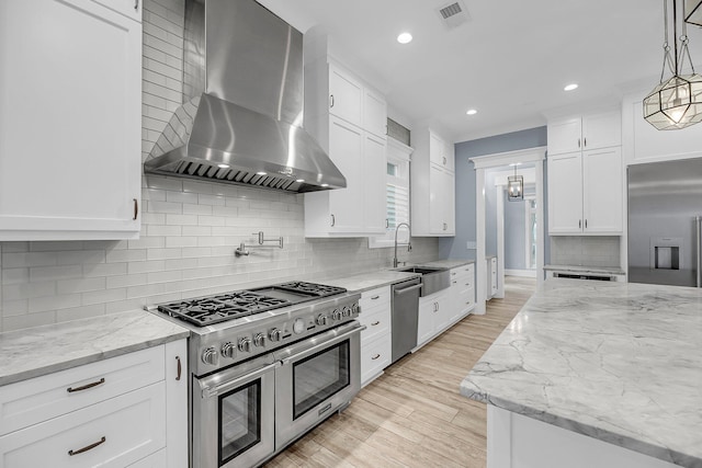 kitchen with high end appliances, visible vents, light wood finished floors, a sink, and wall chimney exhaust hood