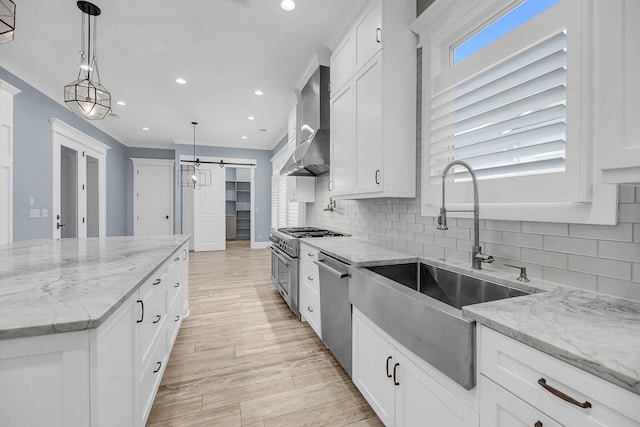 kitchen featuring a sink, white cabinetry, appliances with stainless steel finishes, wall chimney range hood, and decorative backsplash