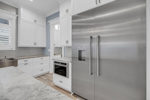 kitchen featuring light stone counters, stainless steel appliances, decorative backsplash, white cabinets, and light wood-type flooring