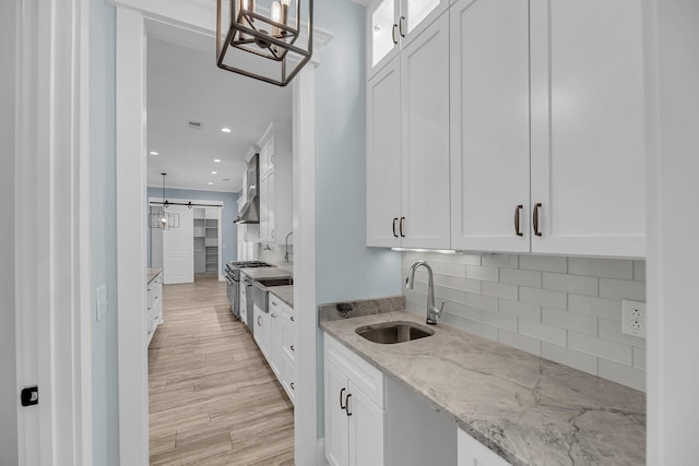 kitchen featuring a sink, light stone counters, white cabinets, and light wood finished floors