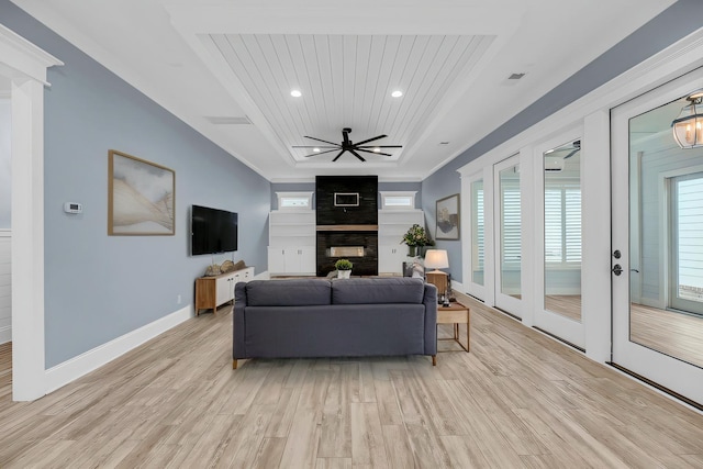 living area featuring baseboards, light wood finished floors, a tray ceiling, recessed lighting, and a multi sided fireplace