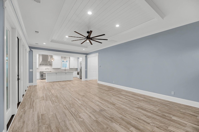 unfurnished living room featuring baseboards, a tray ceiling, recessed lighting, light wood-style flooring, and a ceiling fan