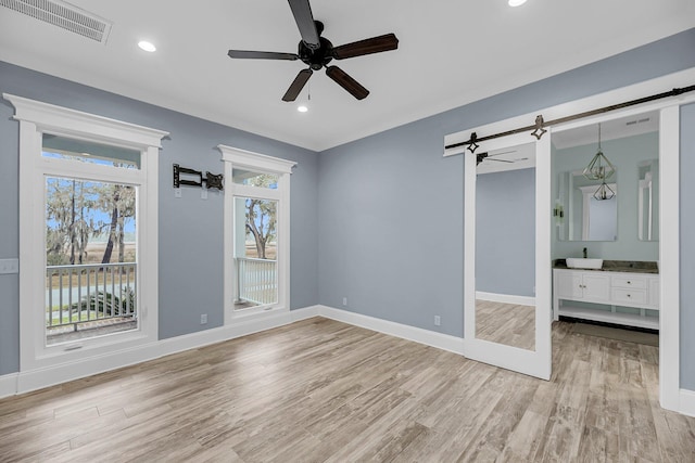 spare room featuring visible vents, baseboards, a barn door, light wood-style floors, and a ceiling fan