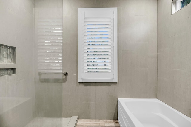 bathroom featuring tile walls, a tub, and a shower