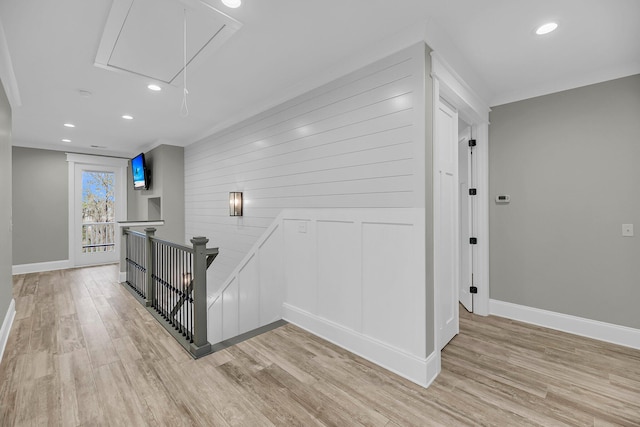 corridor featuring baseboards, an upstairs landing, light wood-style floors, and attic access