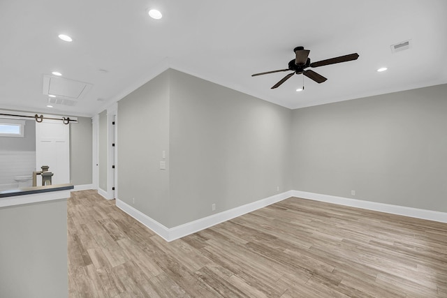 unfurnished room with visible vents, a ceiling fan, light wood-style floors, baseboards, and attic access