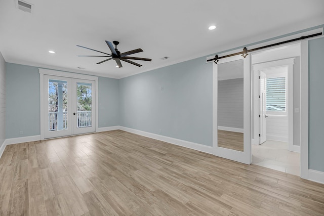 spare room with light wood-type flooring, visible vents, a barn door, french doors, and ceiling fan