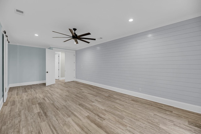 unfurnished room featuring a barn door, light wood-type flooring, visible vents, and ceiling fan