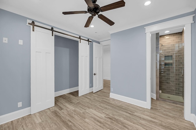 unfurnished bedroom with recessed lighting, a barn door, light wood finished floors, baseboards, and ceiling fan