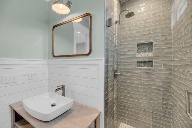 full bath featuring a sink, wainscoting, and a tile shower