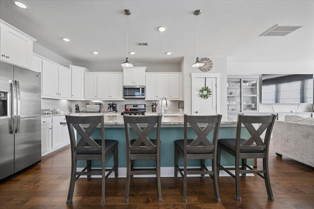 kitchen with a kitchen island with sink, stainless steel appliances, light stone counters, white cabinetry, and decorative light fixtures