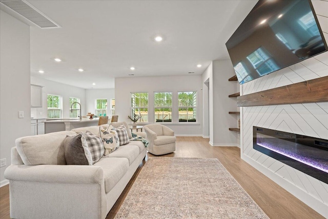 living room featuring a wealth of natural light, a large fireplace, light wood-style flooring, and recessed lighting