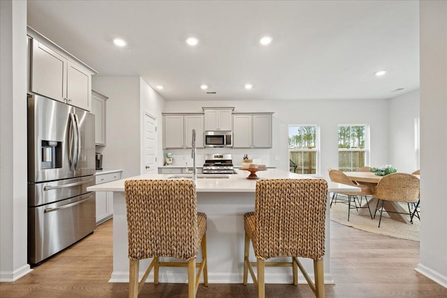 kitchen with a kitchen breakfast bar, light countertops, stainless steel appliances, light wood-type flooring, and a sink