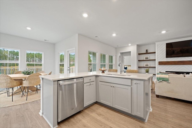 kitchen featuring a sink, light wood-style floors, open floor plan, light countertops, and stainless steel dishwasher