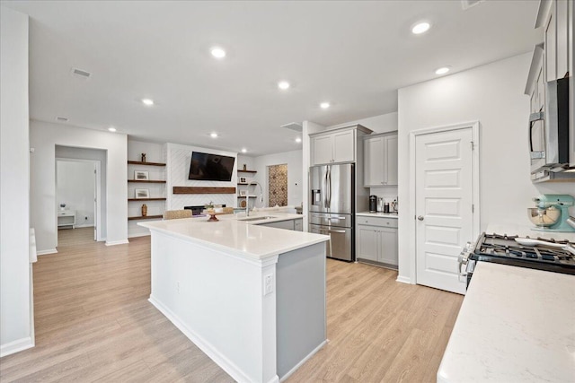 kitchen with a fireplace, light wood finished floors, gray cabinets, light countertops, and stainless steel fridge