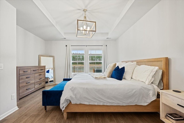 bedroom featuring baseboards, visible vents, wood finished floors, a tray ceiling, and a notable chandelier