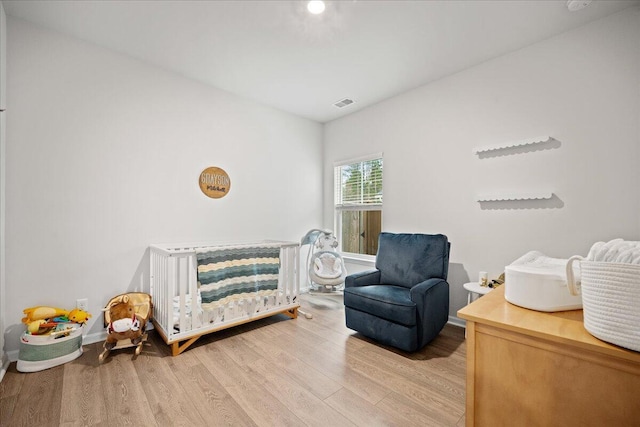 bedroom with a crib, wood finished floors, visible vents, and baseboards