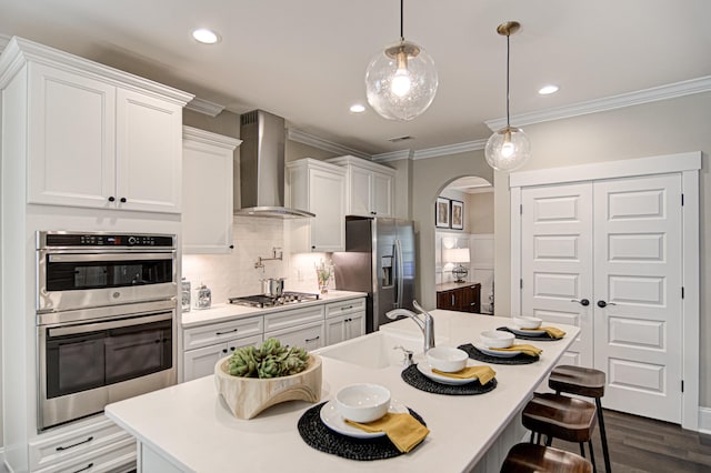 kitchen with sink, wall chimney range hood, decorative light fixtures, white cabinets, and appliances with stainless steel finishes