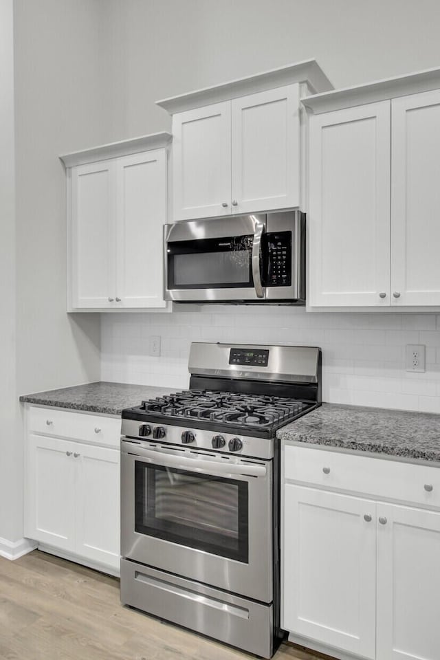 kitchen with tasteful backsplash, light hardwood / wood-style flooring, appliances with stainless steel finishes, dark stone counters, and white cabinets