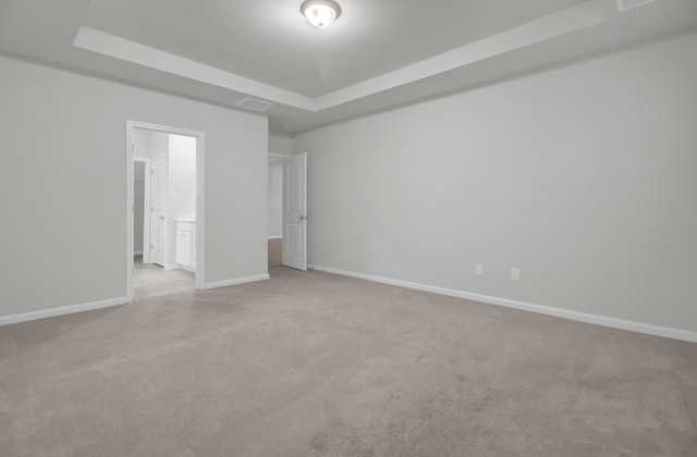 unfurnished bedroom with a tray ceiling, ensuite bath, and light colored carpet