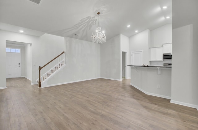 unfurnished living room with high vaulted ceiling, a chandelier, and light hardwood / wood-style floors