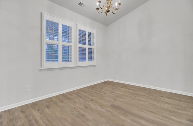 empty room with vaulted ceiling, hardwood / wood-style floors, and an inviting chandelier