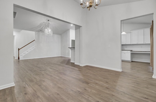 unfurnished living room featuring high vaulted ceiling, a chandelier, and light wood-type flooring