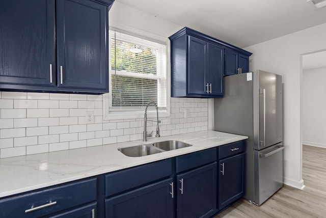 kitchen with decorative backsplash, stainless steel fridge, sink, blue cabinetry, and light hardwood / wood-style floors