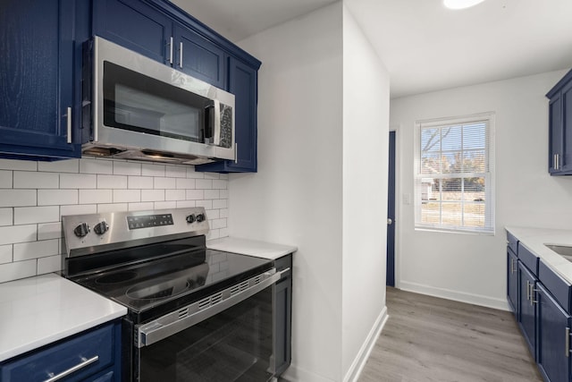 kitchen featuring blue cabinetry, decorative backsplash, stainless steel appliances, and light wood-type flooring