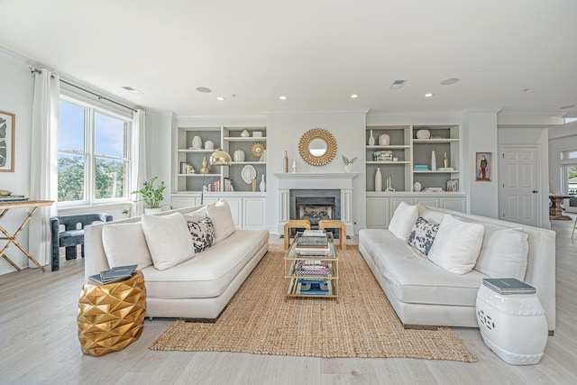 living room with visible vents, ornamental molding, light wood-type flooring, built in shelves, and a high end fireplace