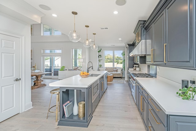 kitchen with visible vents, light countertops, hanging light fixtures, high end stainless steel range oven, and an island with sink