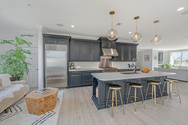 kitchen featuring built in fridge, under cabinet range hood, a sink, open floor plan, and a center island with sink