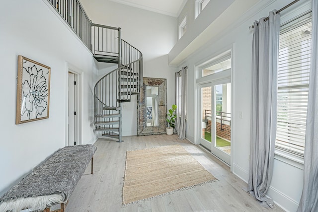 foyer featuring light wood-style flooring, a towering ceiling, baseboards, ornamental molding, and stairway