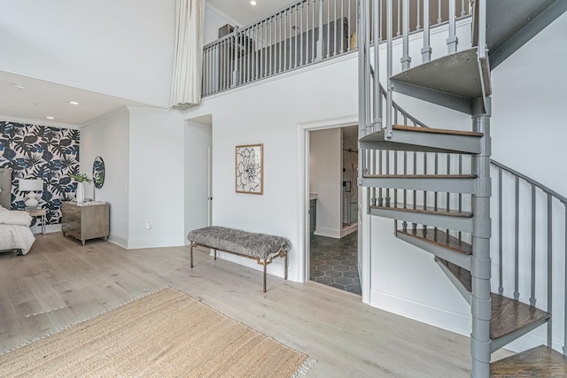 stairway featuring a high ceiling, ornamental molding, and wood finished floors