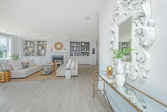 living room featuring built in features, a high end fireplace, crown molding, and light wood-style flooring