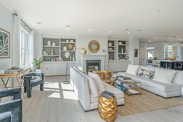 living area with light wood finished floors, visible vents, a premium fireplace, and ornamental molding