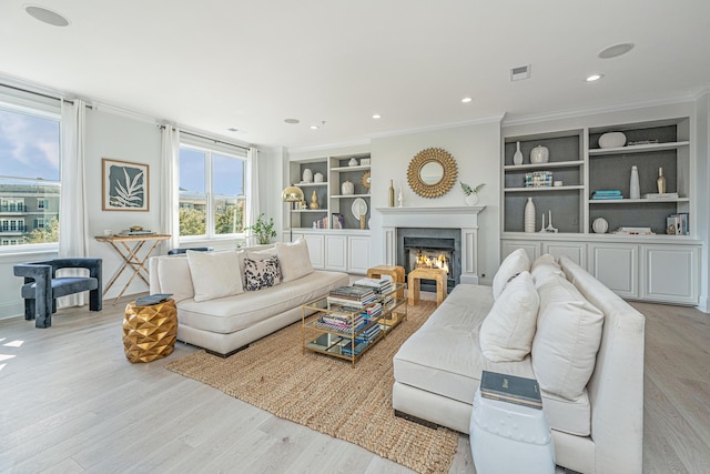 living room featuring built in shelves, visible vents, crown molding, and light wood-style flooring