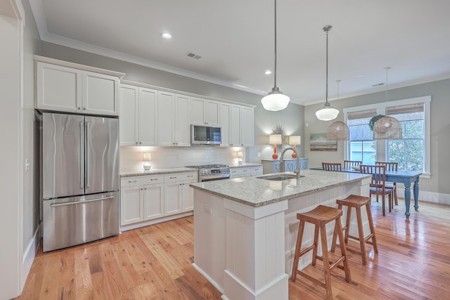 kitchen with pendant lighting, sink, appliances with stainless steel finishes, white cabinets, and a center island with sink