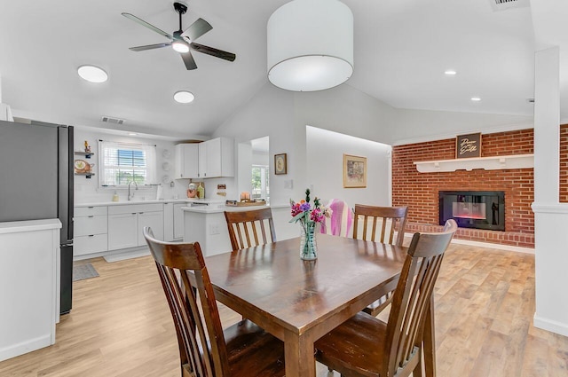 dining space featuring vaulted ceiling, ceiling fan, light wood finished floors, a fireplace, and recessed lighting