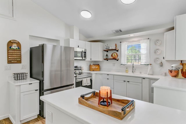 kitchen with stainless steel appliances, a sink, vaulted ceiling, visible vents, and white cabinetry