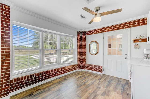 entryway with brick wall, wood finished floors, visible vents, and crown molding