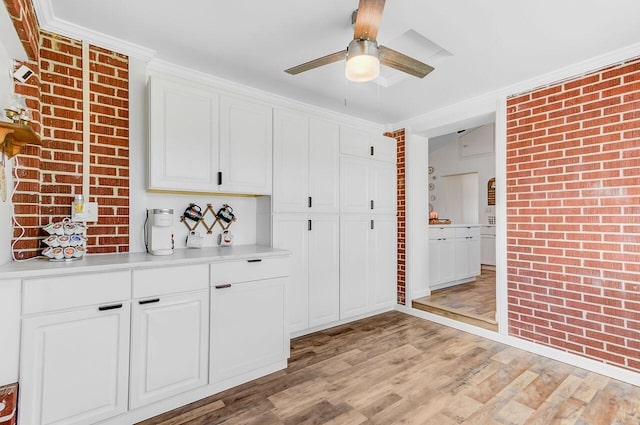kitchen featuring brick wall, light wood finished floors, ceiling fan, and light countertops