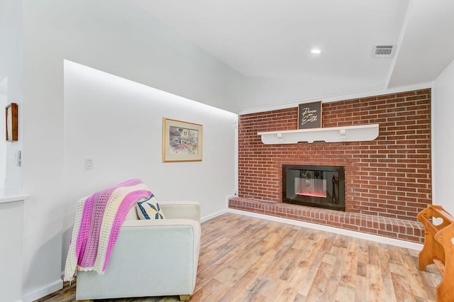 living area featuring wood finished floors, baseboards, a brick fireplace, and visible vents