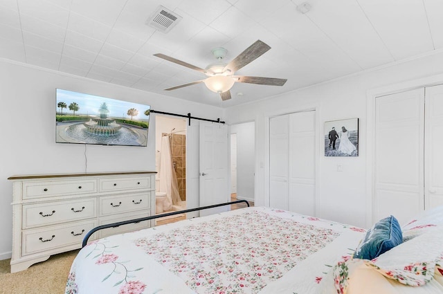 bedroom featuring a barn door, multiple closets, visible vents, a ceiling fan, and connected bathroom