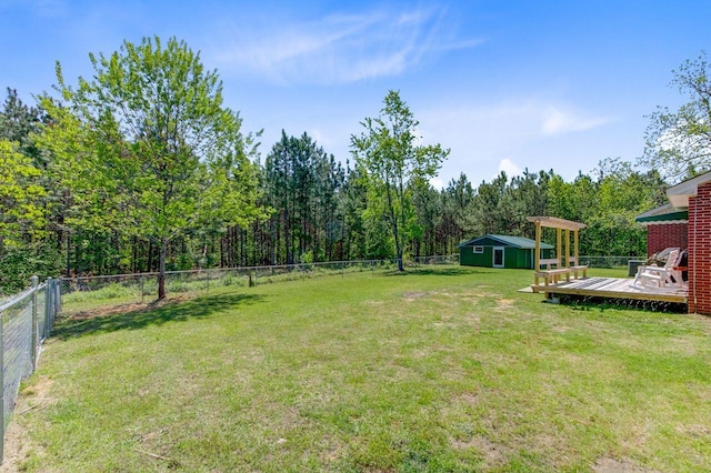 view of yard with a fenced backyard, an outbuilding, a forest view, and a deck