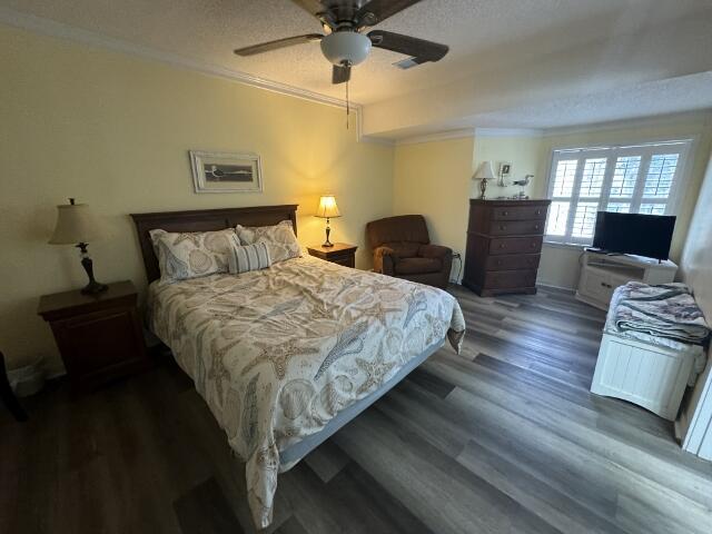 bedroom with dark wood-style floors, a textured ceiling, a ceiling fan, and crown molding