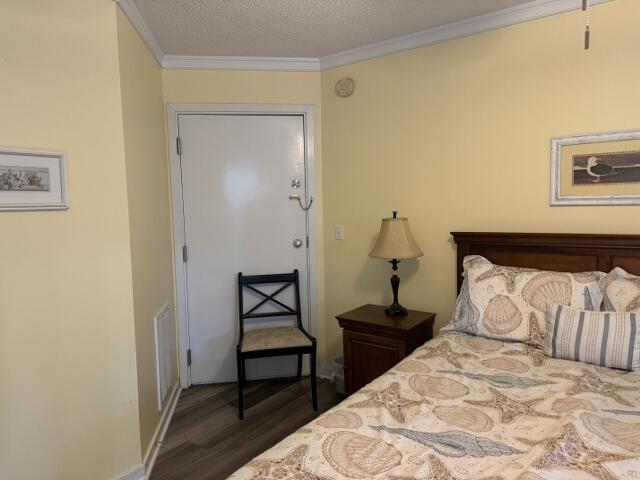 bedroom featuring dark wood-style floors, a textured ceiling, visible vents, and crown molding