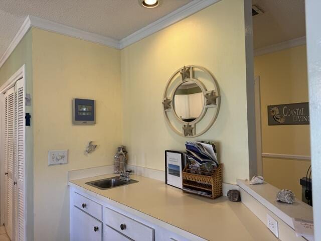 kitchen with ornamental molding, white cabinets, light countertops, and a sink